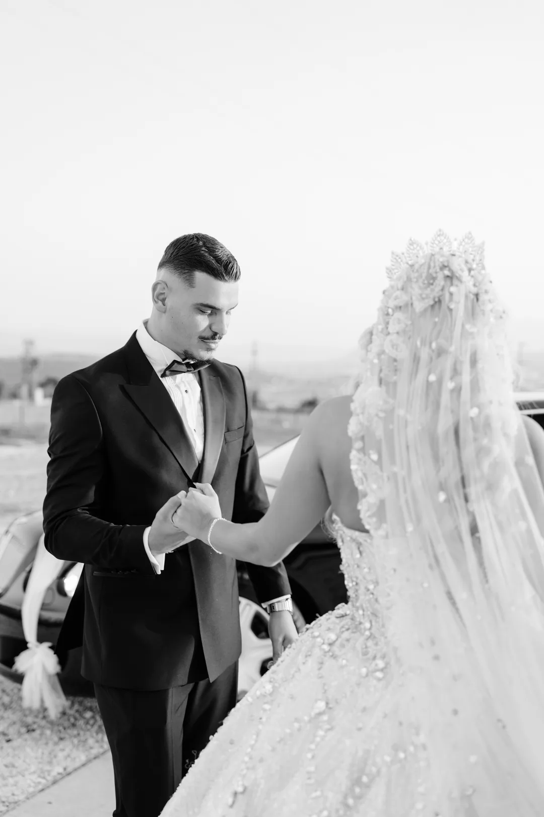 Groom taking the bride's hand as she arrives, her crystal veil in the foreground, in black and white