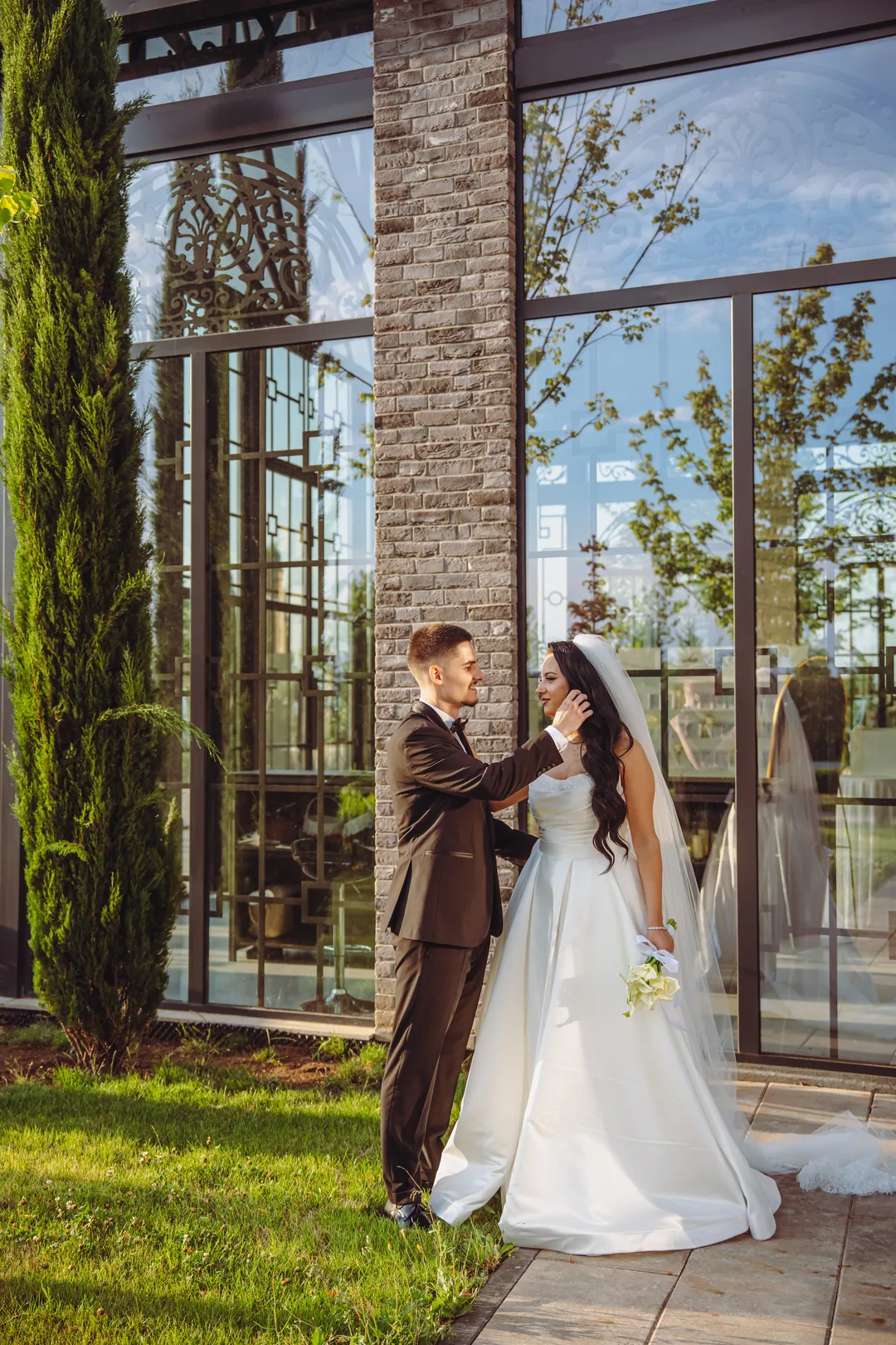 Groom touching the bride's veil in front of the pavilion's tall windows