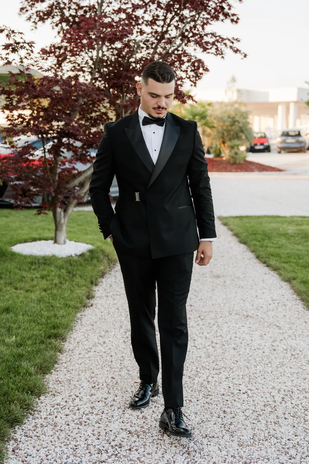 Groom walking down a gravel path in a double-breasted tuxedo