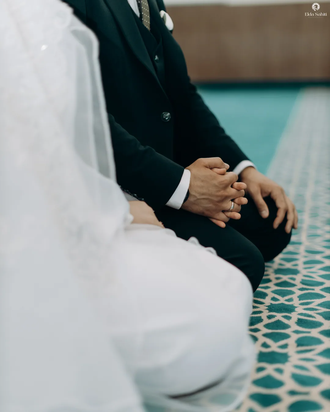 Groom's clasped hands beside the bride's white dress as they kneel in the mosque