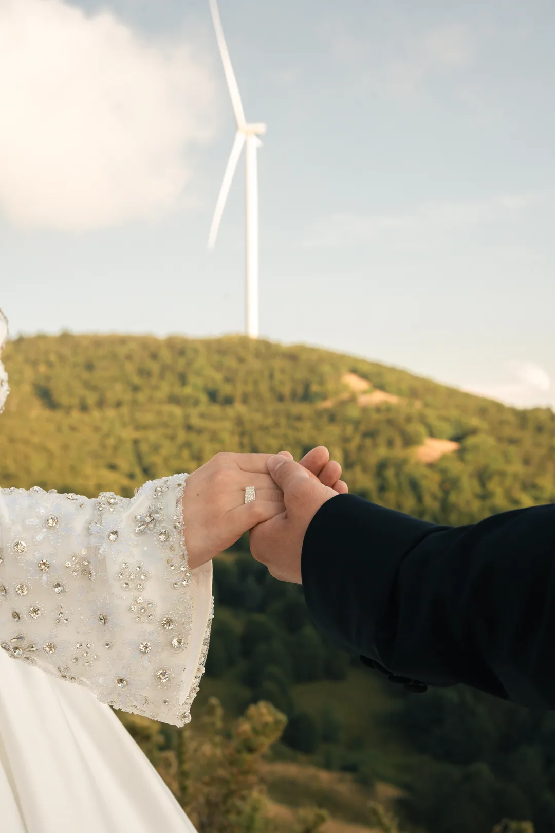 Bride and groom holding hands against green hills and a wind turbine