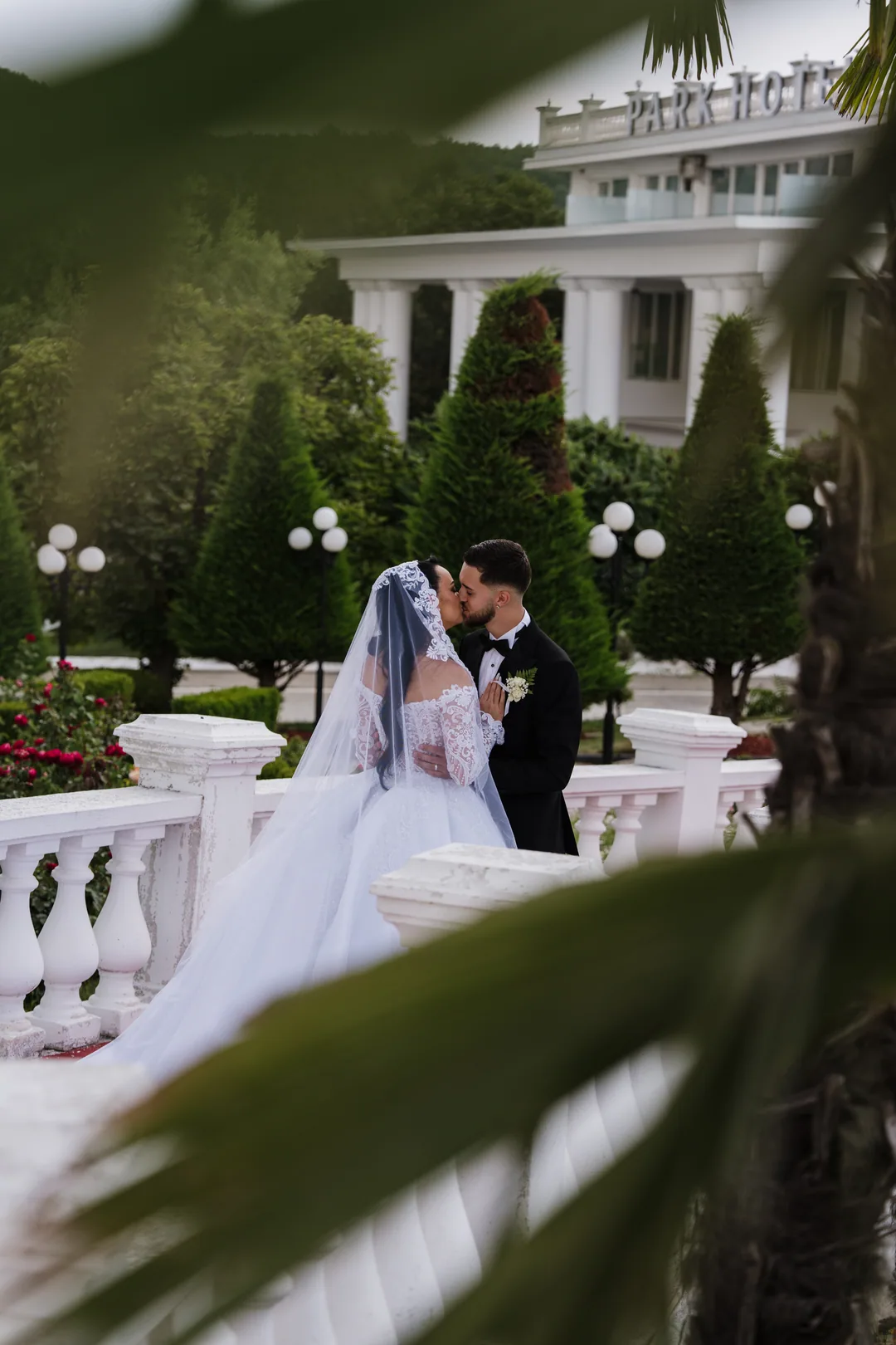 Couple kissing at a white balustrade, framed by palm leaves