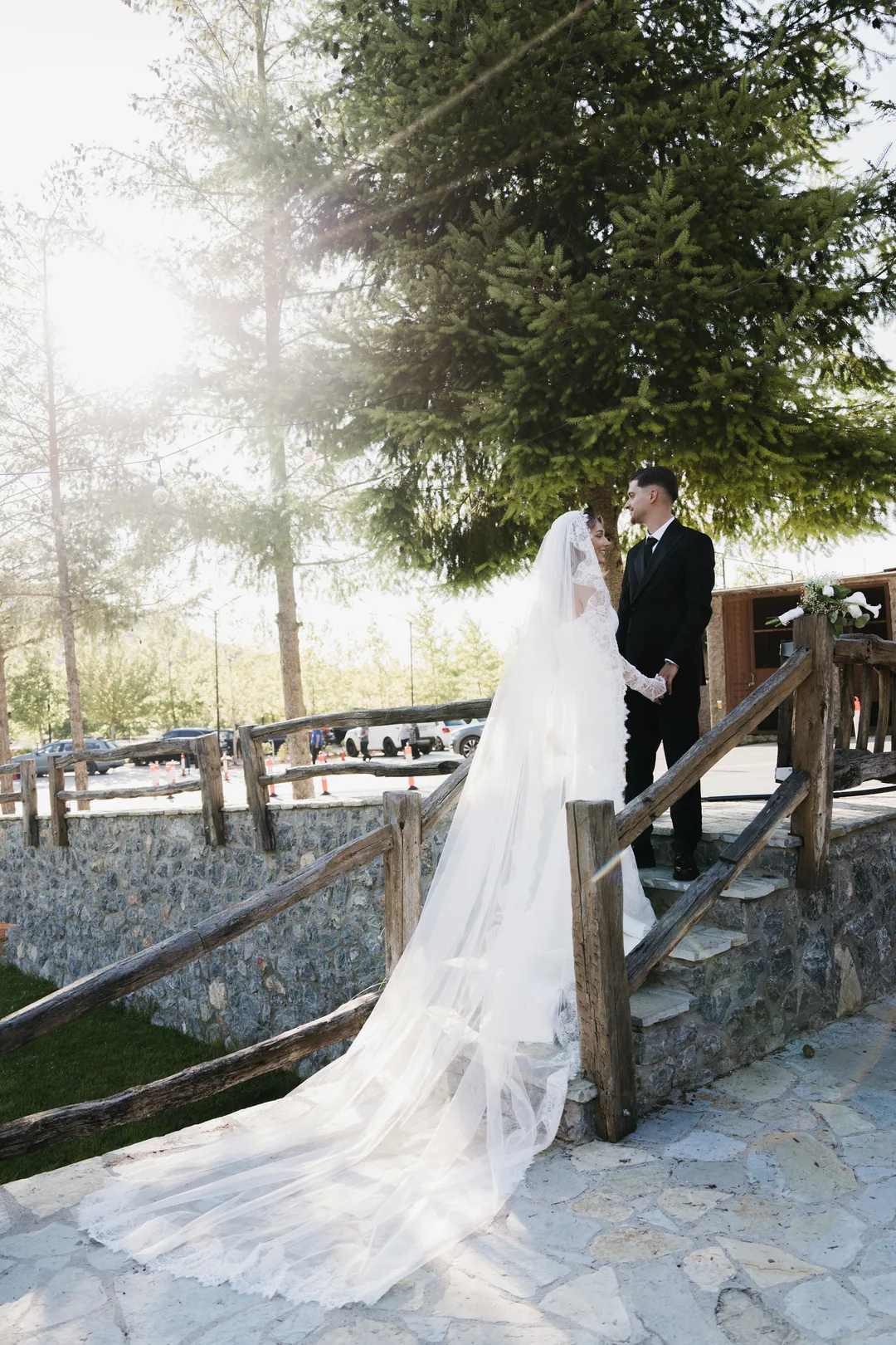 Couple kissing at the top of rustic stone steps, her veil trailing down them in the sun