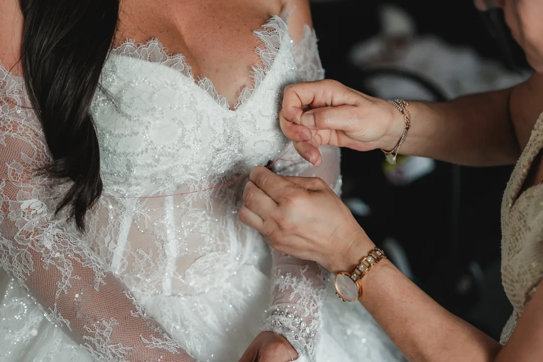 A pair of hands adjusting the lace bodice of the bride's gown