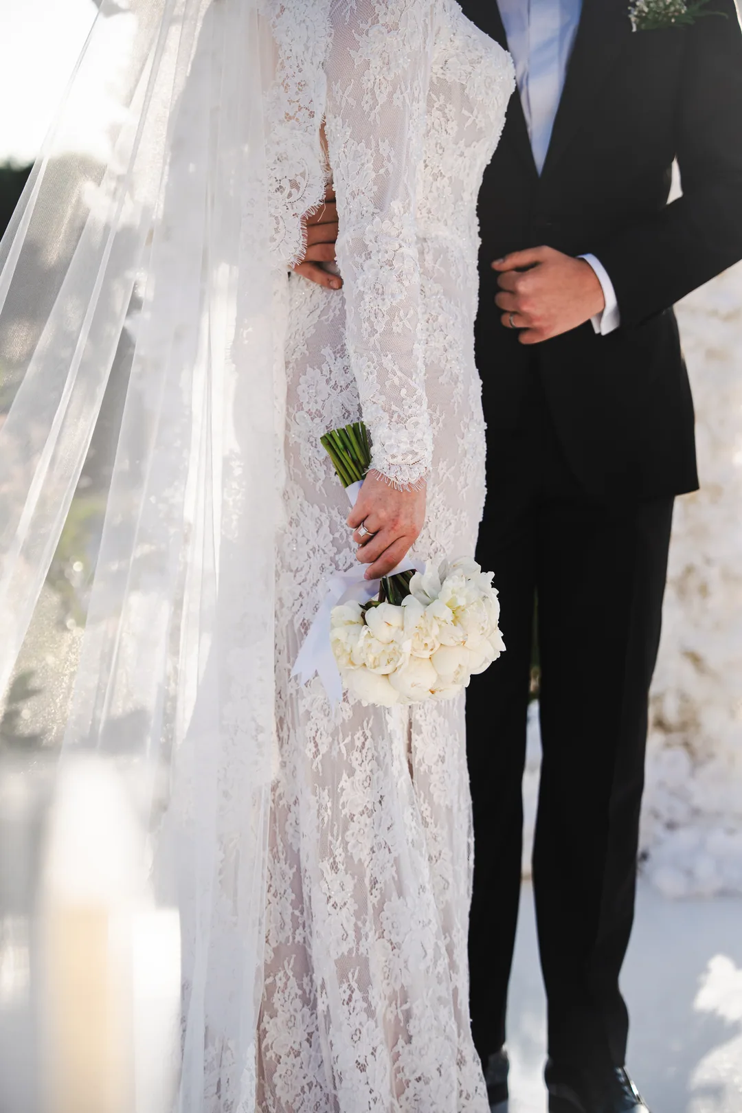 Lace gown and a bouquet of white roses, the groom's hands beside her