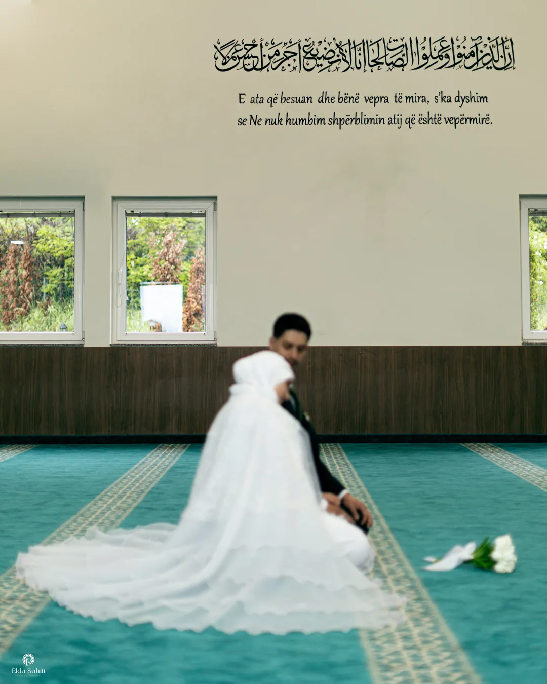 Bride and groom kneeling on the turquoise carpet of a mosque