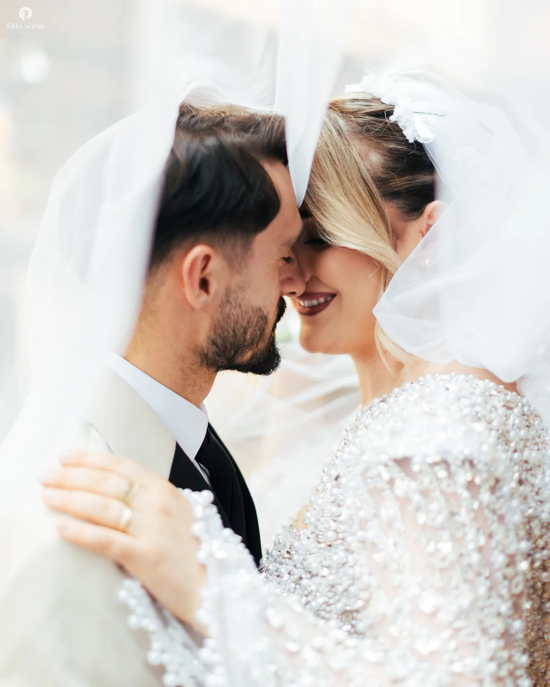 Nose to nose under the veil, her pearl-covered sleeve on his shoulder