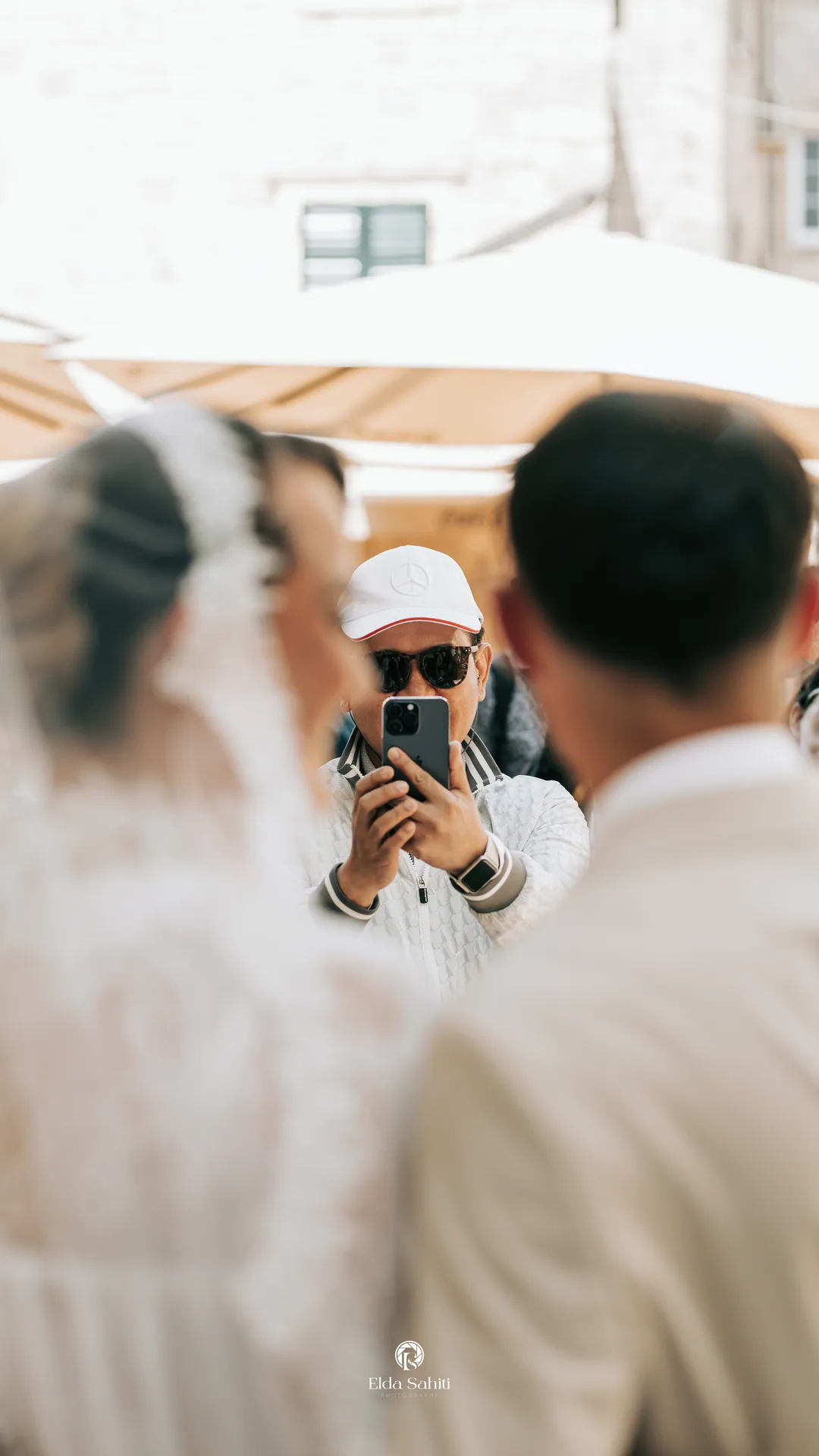 A passer-by in a cap photographing the couple on his phone