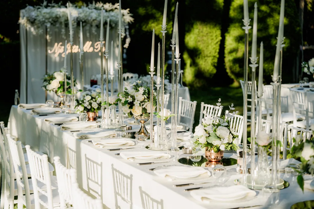 Long reception table set outdoors with tall candlesticks and white flowers
